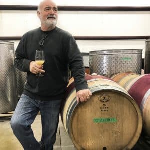 Derek Barnett, Winemaker at Karlo Estates Winery leans back on a barrel, glass in hand.